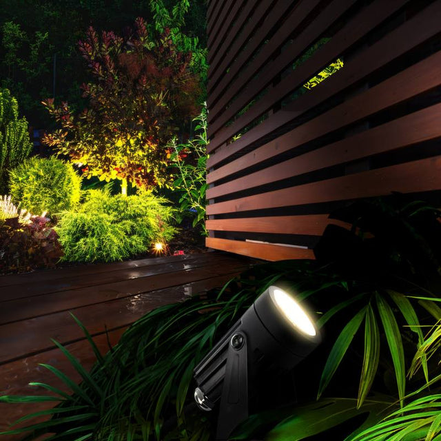 "Outdoor spotlight illuminating a garden at night, showcasing its spike-mounted design and adjustable head."