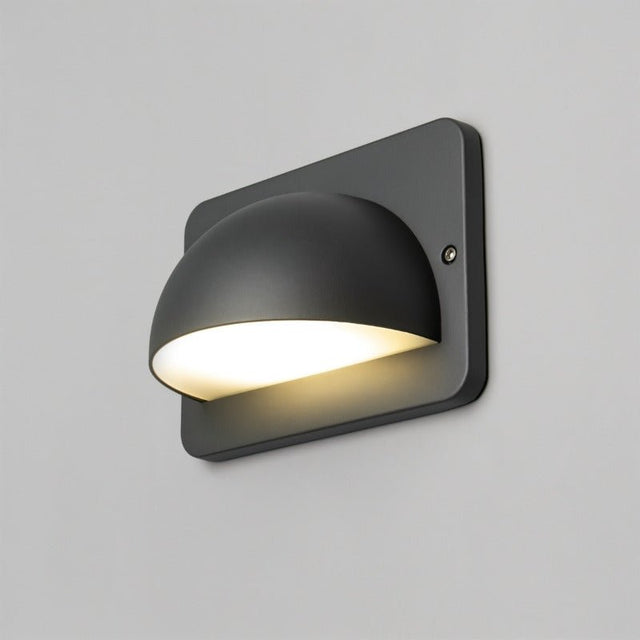 "A modern, dome-shaped outdoor wall lamp casting a soft, downward light on a light gray wall."