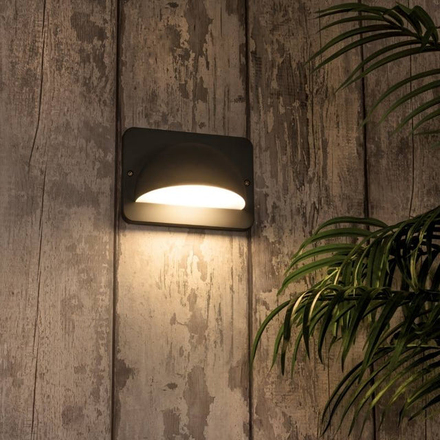 "A modern, dome-shaped outdoor wall lamp casting a soft glow on a weathered wooden wall."