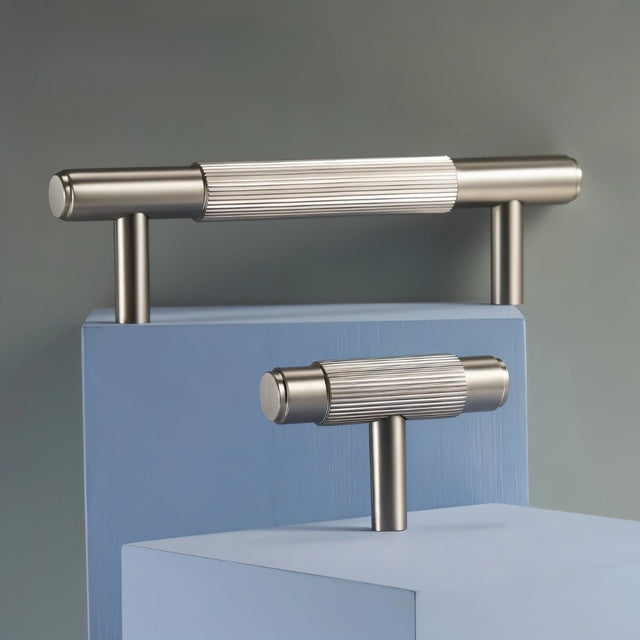 "Modern brass drawer knobs and pull bars with a textured, knurled grip on a blue and gray background."