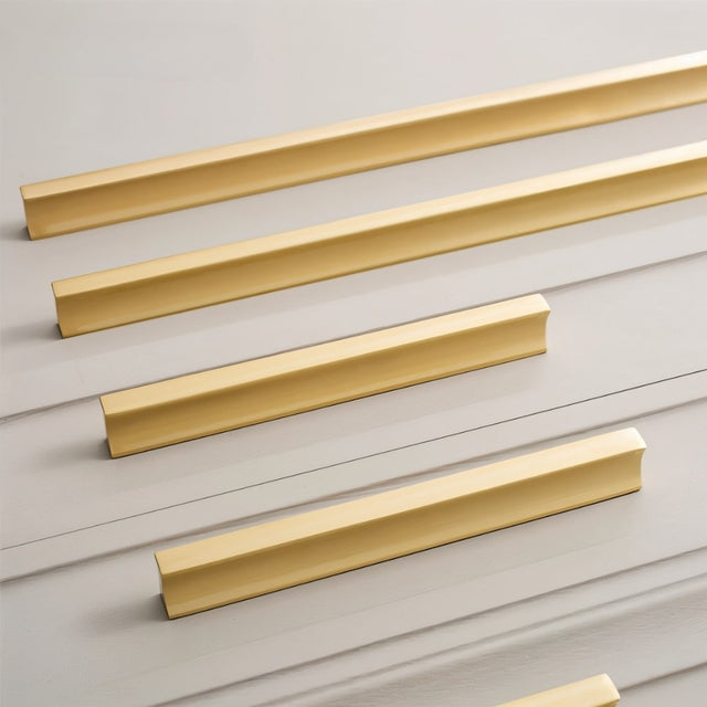 "Arrangement of sleek geometric brushed brass pull bars on modern gray kitchen cabinets."