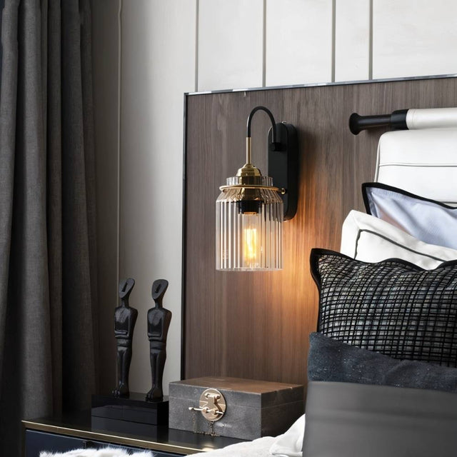 "A brass wall lamp with a ribbed glass shade in a bedroom setting."