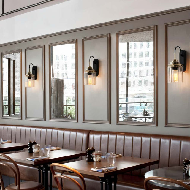 "Brass wall lamps with ribbed glass shades lining a restaurant wall with mirrors."