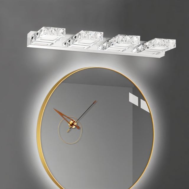 "A modern crystal wall sconce mounted above a round, gold-framed mirror with a clock face in a dimly lit bathroom."