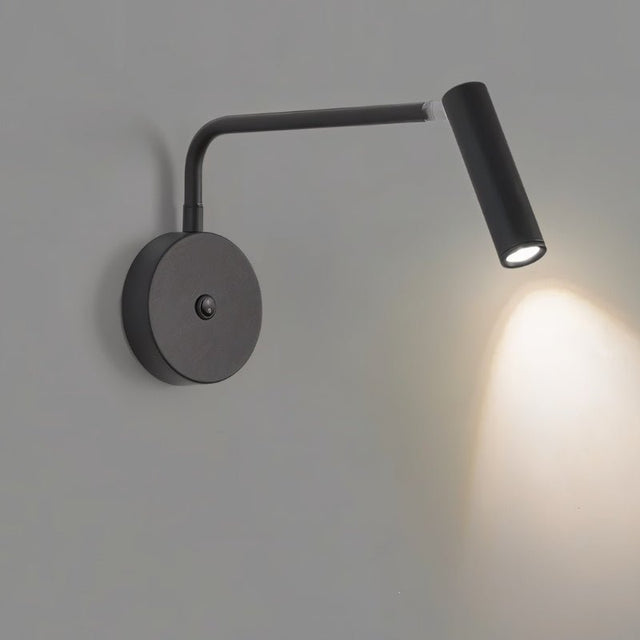 "A black wall lamp with a pivoting arm and cylindrical head, lit up on a gray wall."