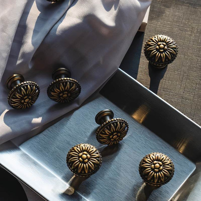"Set of antique brass floral knobs with raised petal detailing on a fabric and metal surface."