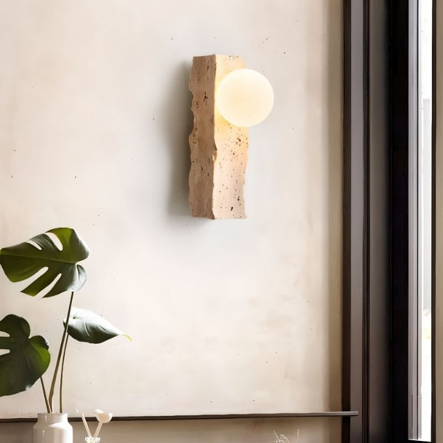 "Minimalist wall lamp with a raw travertine base and frosted glass globe, mounted on a neutral-toned wall"
