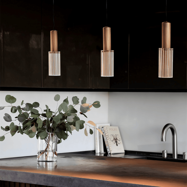 Set of Nayra Copper Glass Pendant Lights above a kitchen counter with black cabinetry and copper-toned surface, perfect for modern interiors.