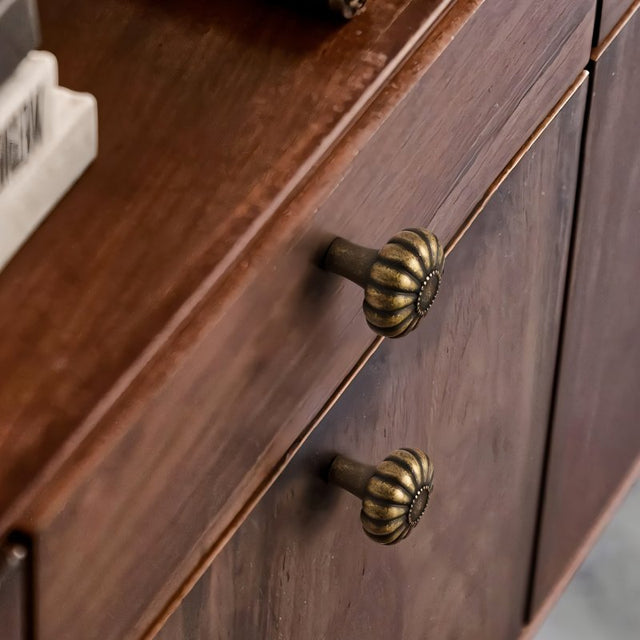 "Two vintage brass flower-shaped knobs with bold, rounded petals, installed on a dark wood dresser, adding an antique appeal to the furniture."