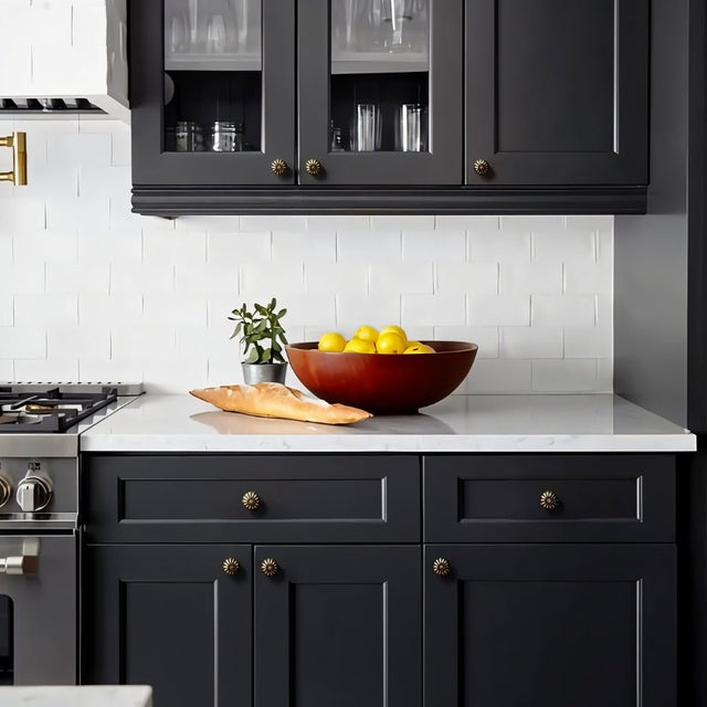 "Vintage brass flower-shaped knobs with bold, rounded petals, installed on dark gray kitchen cabinets, complementing the white countertop and backsplash."