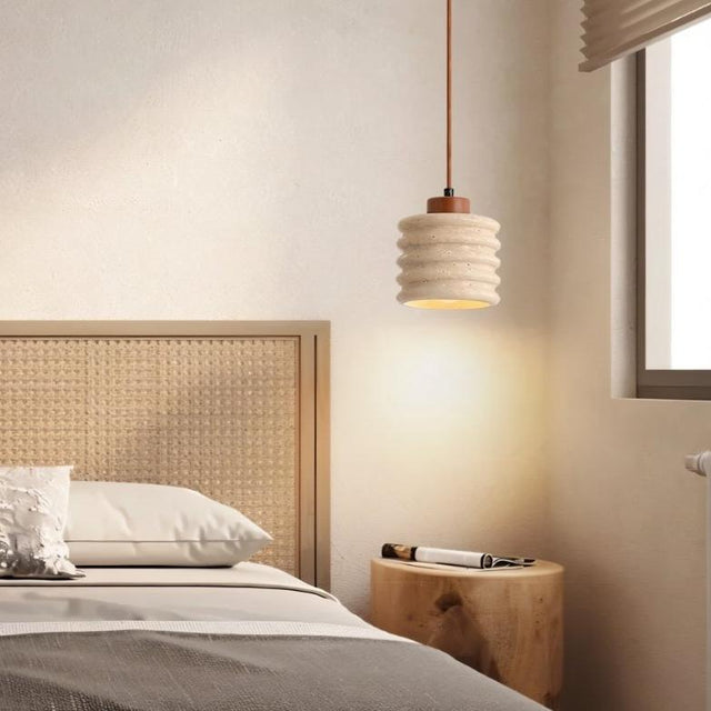 "A travertine pendant light with a ribbed design hanging over a bedside table in a bedroom."