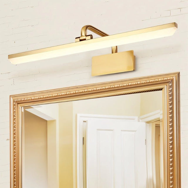 "A gold-finish LED vanity light mounted above an ornate gold-framed mirror on a textured wall."