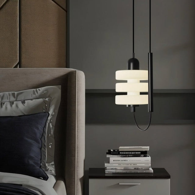 "Modern pendant light with layered frosted glass diffuser and black iron frame, hanging above a bedside table in a bedroom."