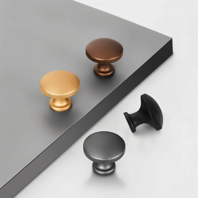 "A set of minimalist cabinet knobs in various metallic finishes, arranged on a grey and white surface."