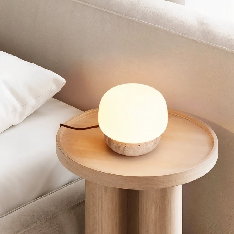 "Softly glowing table lamp with a travertine base on a wooden bedside table"