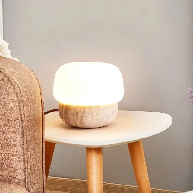 "Modern table lamp with a travertine base and glass shade on a wooden side table"
