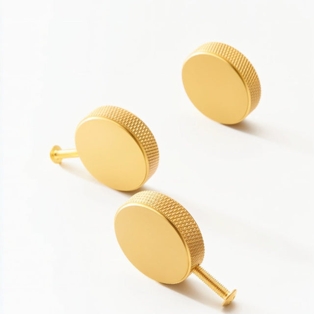 "Three gold brass cylindrical knobs with knurled texture on a white surface."