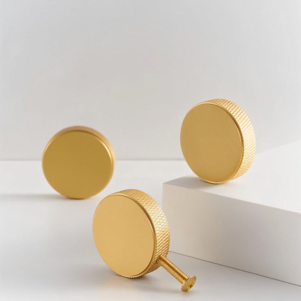 "Three gold brass cylindrical knobs with knurled texture on a white and gray background, showcasing a modern design."