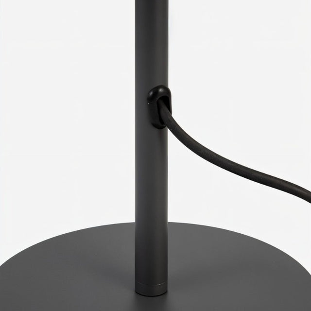 "A close-up view of the black base and cord of a white table lamp with a layered, wave-like diffuser."