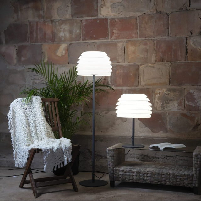 "A layered white table lamp with a wave-like shade, next to a matching floor lamp, in a rustic indoor setting."