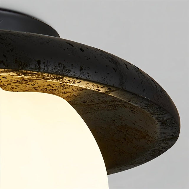 "A close-up view of a ceiling light with a black travertine frame and a cloud-shaped, white acrylic shade, showing the texture of the travertine."