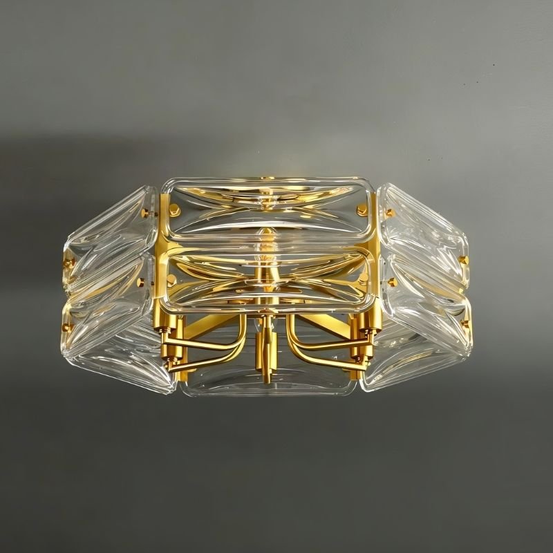 "An angled view of a modern flush mount ceiling light with a geometric glass shade and gold frame, against a dark background."