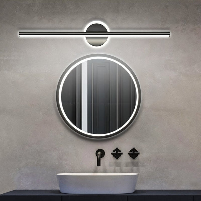 "A modern black wall lamp with a cylindrical bar intersecting a circular base, mounted above a round mirror in a contemporary bathroom with a white vessel sink and gray walls."