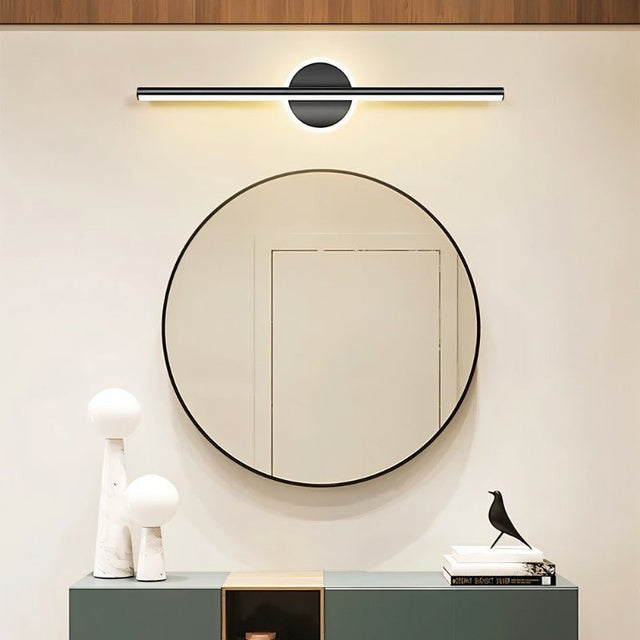 "A modern black wall lamp with a cylindrical bar intersecting a circular base, mounted above a round mirror in a contemporary bathroom with a minimalist aesthetic."