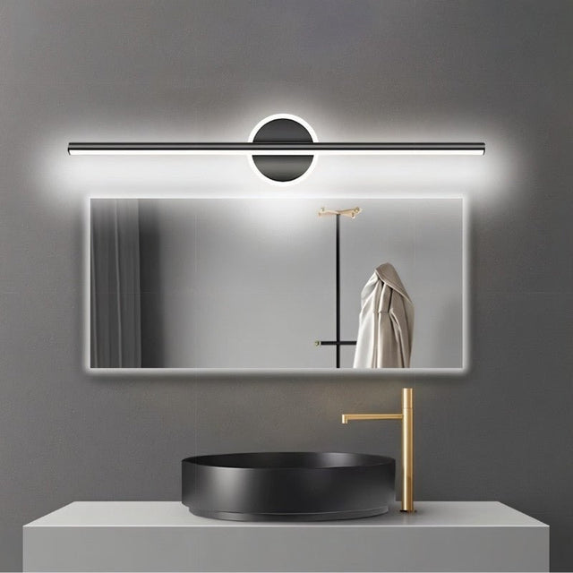 "A modern black wall lamp with a cylindrical bar intersecting a circular base, mounted above a rectangular mirror in a contemporary bathroom with a black vessel sink."