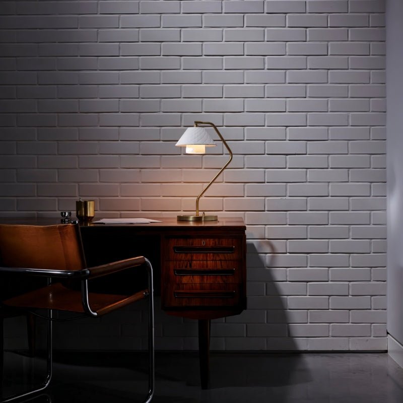 Ocris Table Lamp illuminating a dark study room with brass body and white ceramic shade, ideal for classical home lighting.