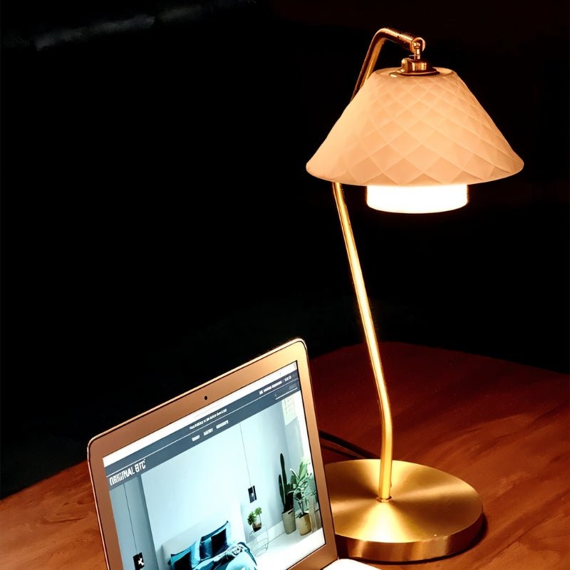 Ocris Table Lamp with brass base and quilted ceramic shade lighting a workspace, perfect for ambient bedroom or office lighting.