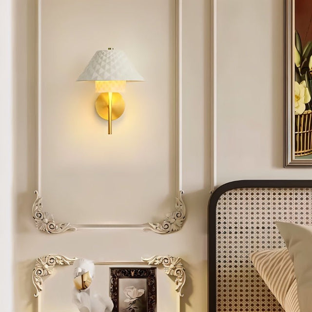 "A modern brass wall lamp with a textured ceramic shade in a bedroom with decorative wall panels."