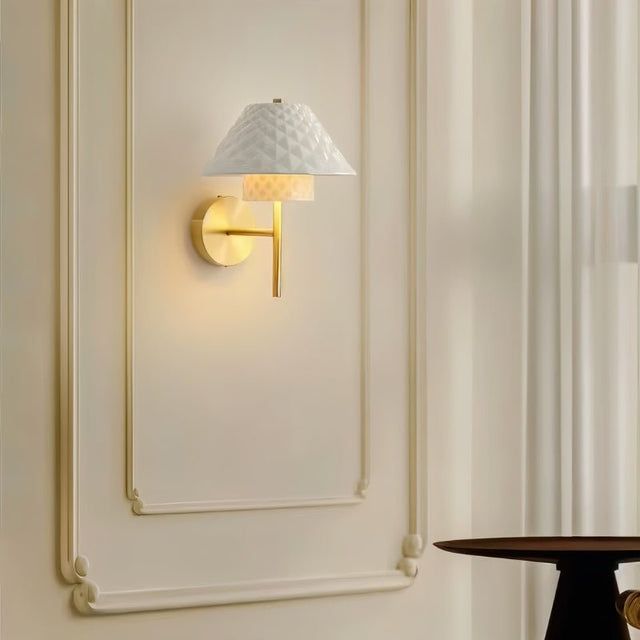"A modern brass wall lamp with a textured ceramic shade on a panelled wall."