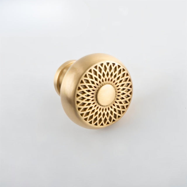 "A gold brass geometric knob with a lattice and sunburst design, shown at an angle on a light background."