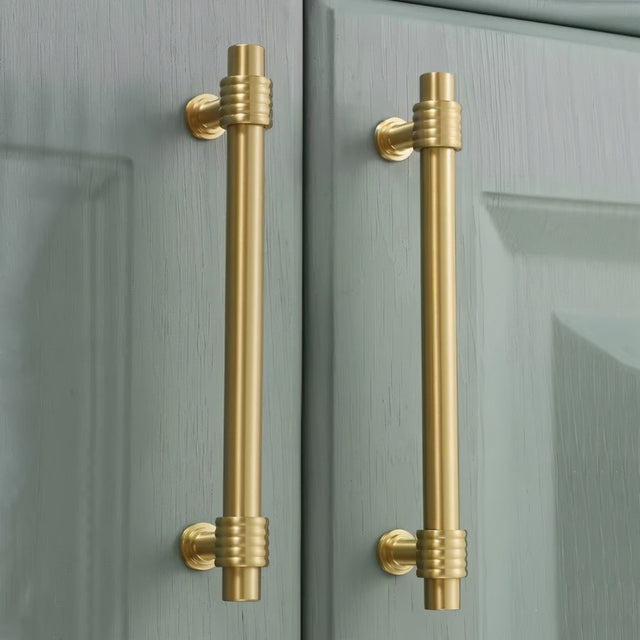 "brass pull bars installed on green kitchen cabinets"