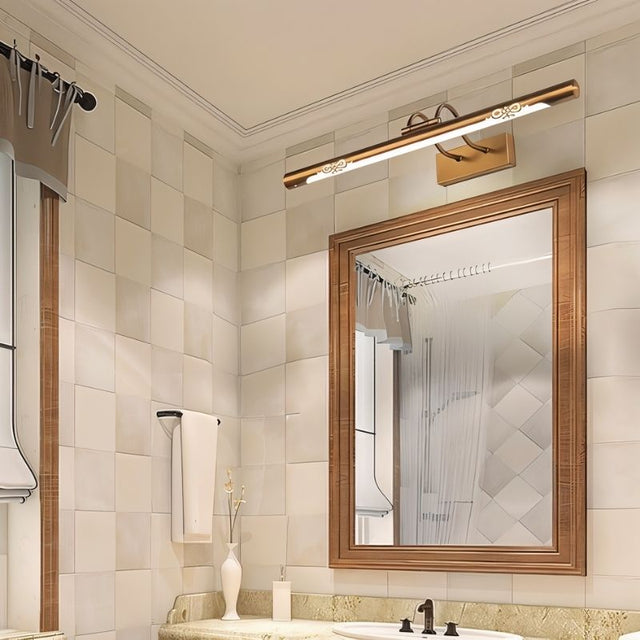 "A copper LED vanity light with decorative cutouts illuminating a bathroom mirror and sink."