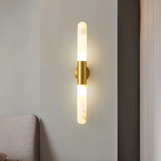 "Modern wall lamp with a gold metallic center and a cylindrical alabaster shade, emitting soft light."