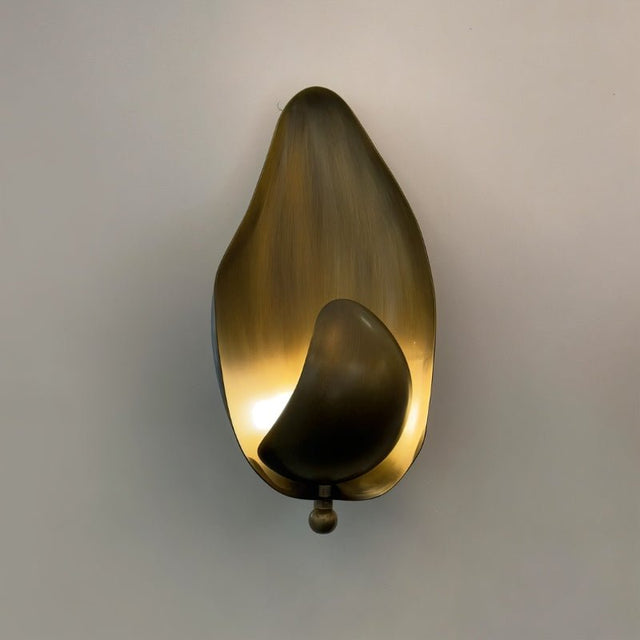 "Lit copper wall lamp with a leaf-inspired design casting a warm glow on a light wall."