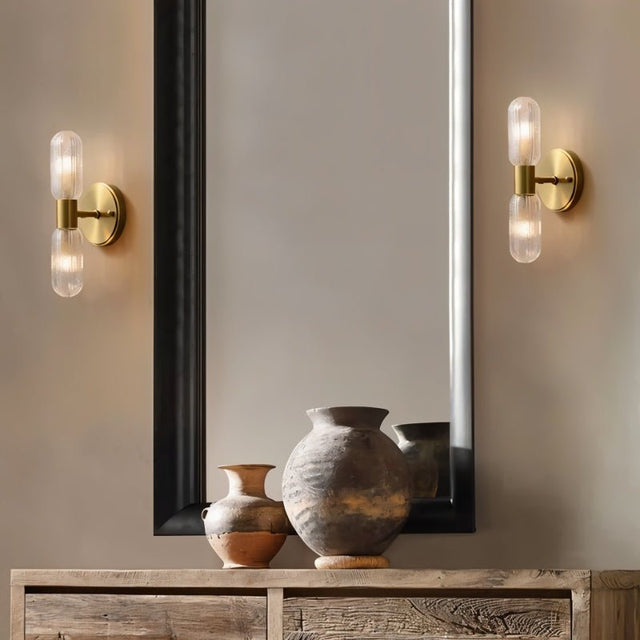 "A pair of modern brass wall lamps with textured glass shades flanking a mirror."