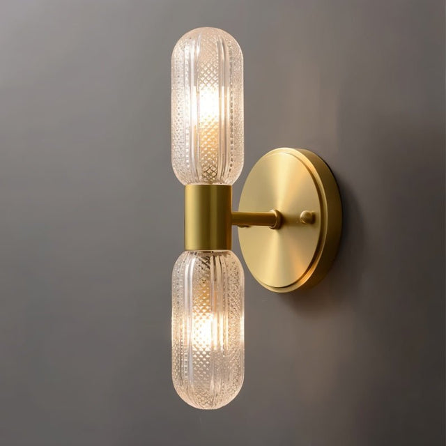 "A modern brass wall sconce with textured glass shades on a gray wall."