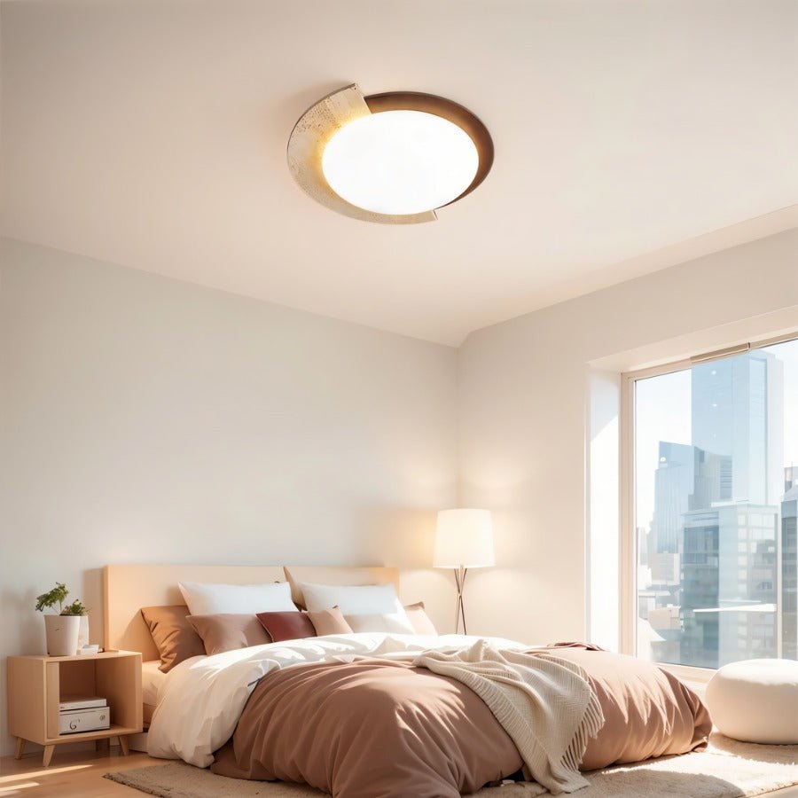 "Wabi-sabi flush mount light with travertine and white diffuser on a bedroom ceiling, providing soft ambient light in a room with a large window overlooking a cityscape."