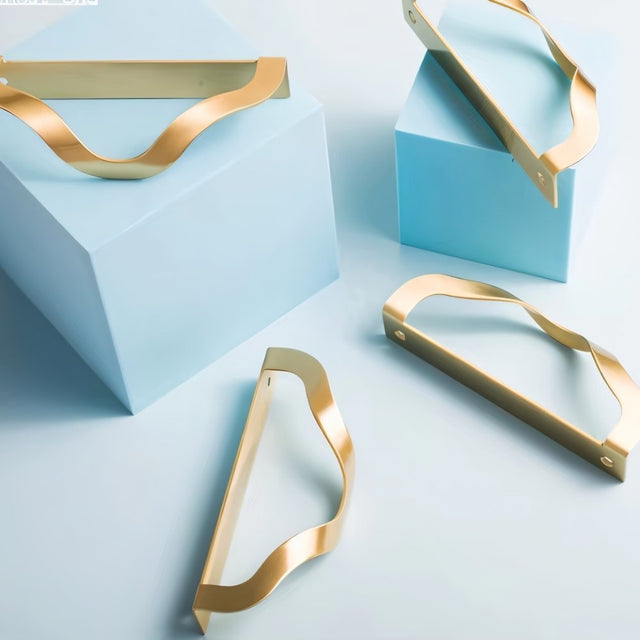 "Lifestyle image showcasing brass drawer pulls with an elegant, wavy design on light blue and white surfaces, suitable for modern or transitional interiors."