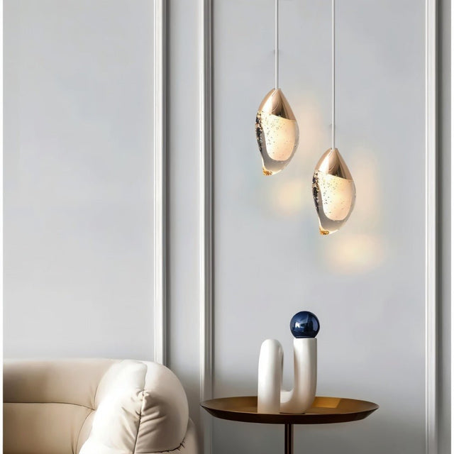 "Pair of modern pendant lights with fluid crystal forms and metal tops in a contemporary living room with a side table."