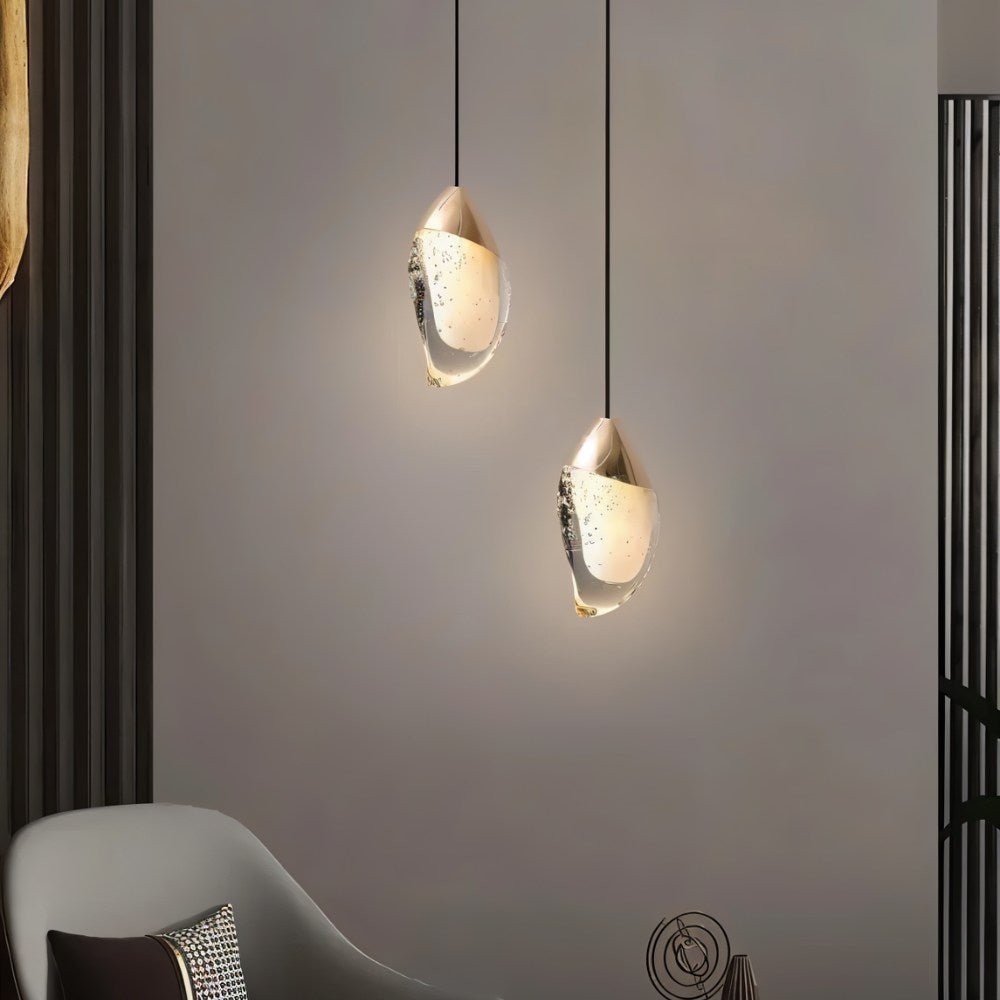 "Pair of modern pendant lights with fluid crystal forms and metal tops in a contemporary living room with a gray armchair."