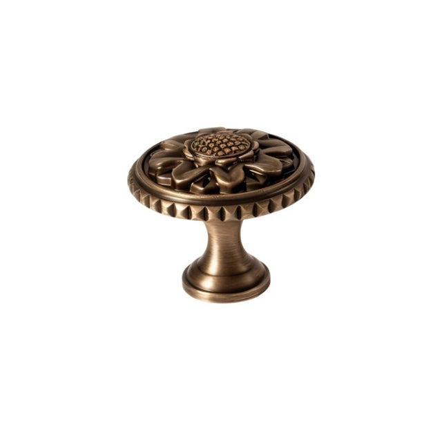"Antique brass floral knob with detailed floral motif and textured border, isolated on a white background."