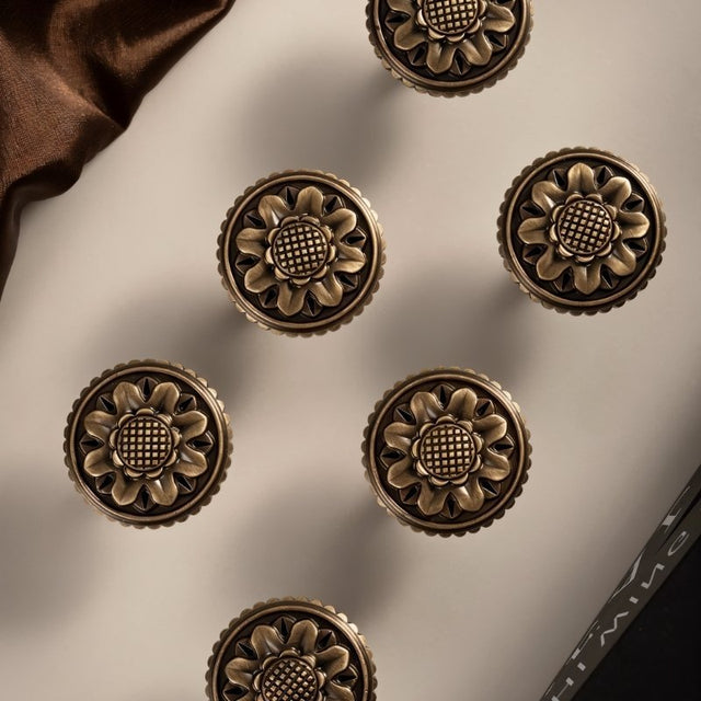 "Set of antique brass floral knobs with detailed floral motif and textured border on a light surface."