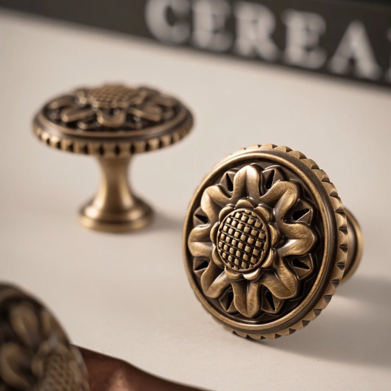 "Two antique brass floral knobs with detailed floral motif and textured border on a light surface."