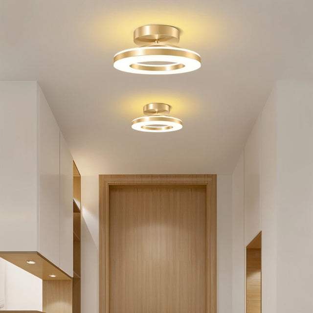 "Two modern circular ceiling lights with gold dual-ring design illuminating a hallway with a wooden door."