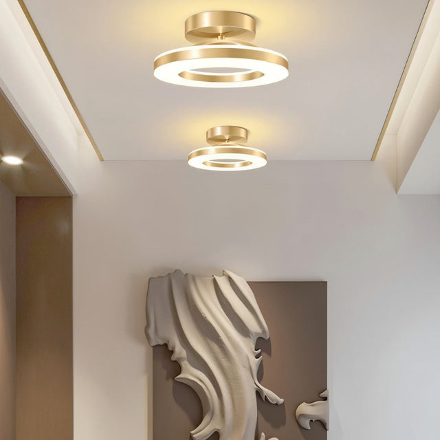 "Two modern circular ceiling lights with gold dual-ring design illuminating a hallway with a wooden door."