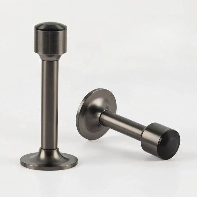 "Two sculpted brass door stops with sleek, tapered silhouettes, polished gunmetal finishes, wide stable bases, and magnetic holds, designed to prevent wall damage."